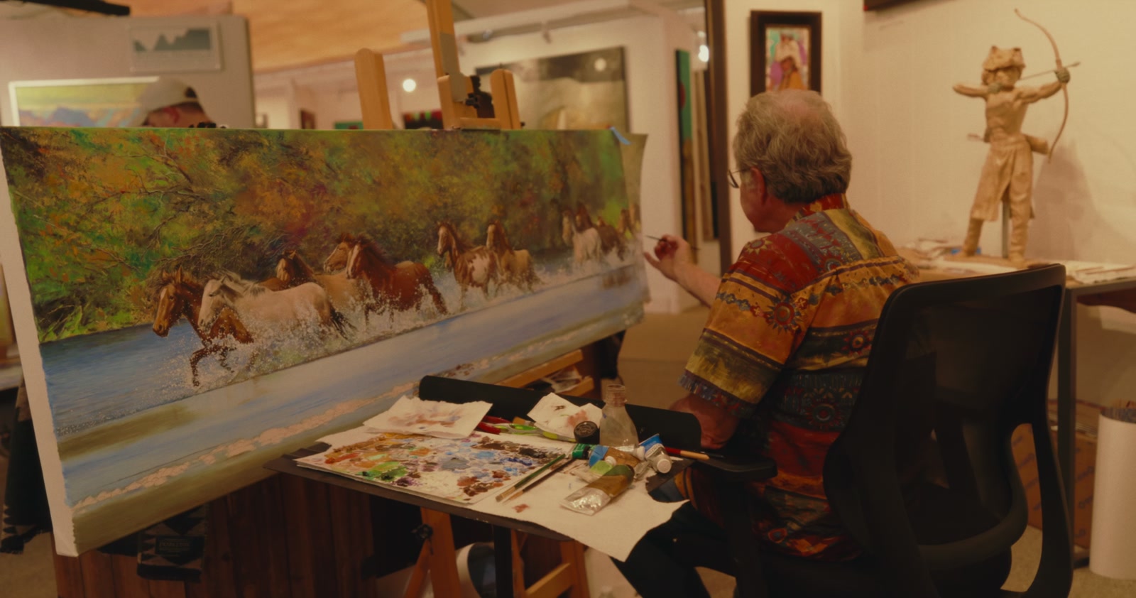 An artist painting a colorful landscape in a working studio
