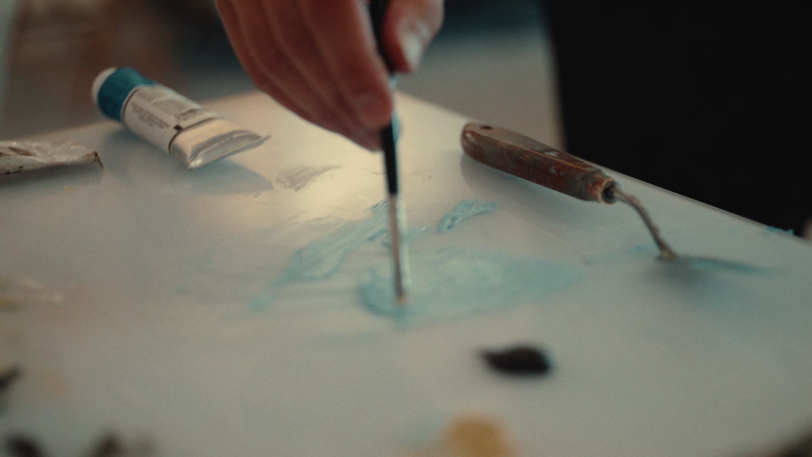 A close view of a painter’s brush moving over a pale blue canvas